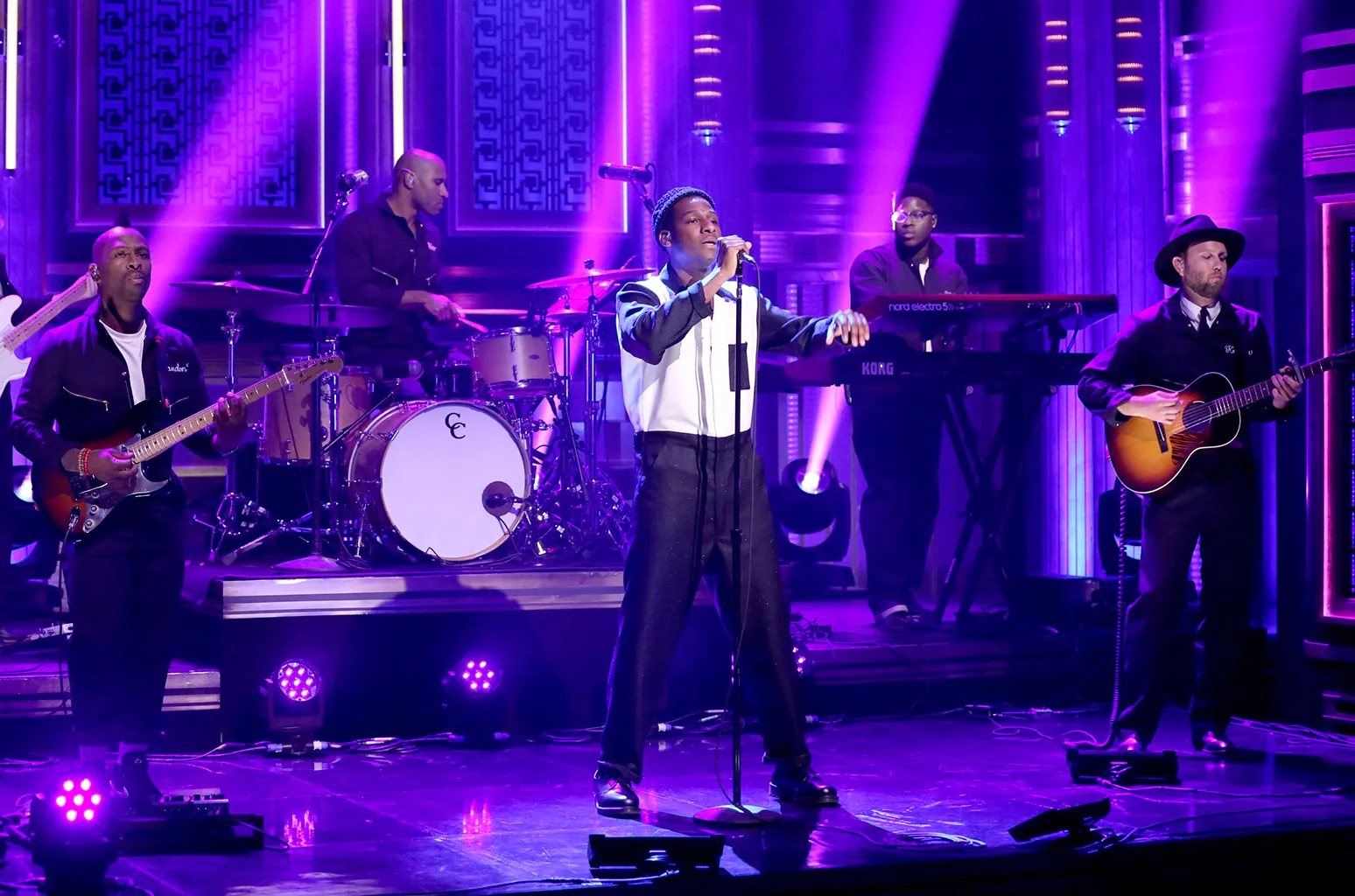 Singer at a microphone with a live band on a purple-lit stage
